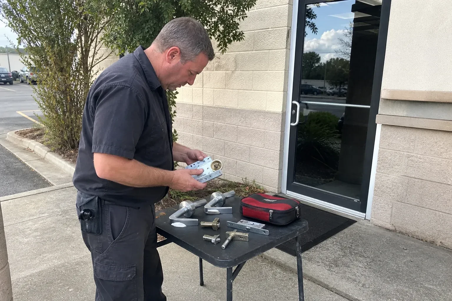 Technician examining detached commercial lock hardware on a table outside a shop entrance. — Business Lockout Service, Kitchener
