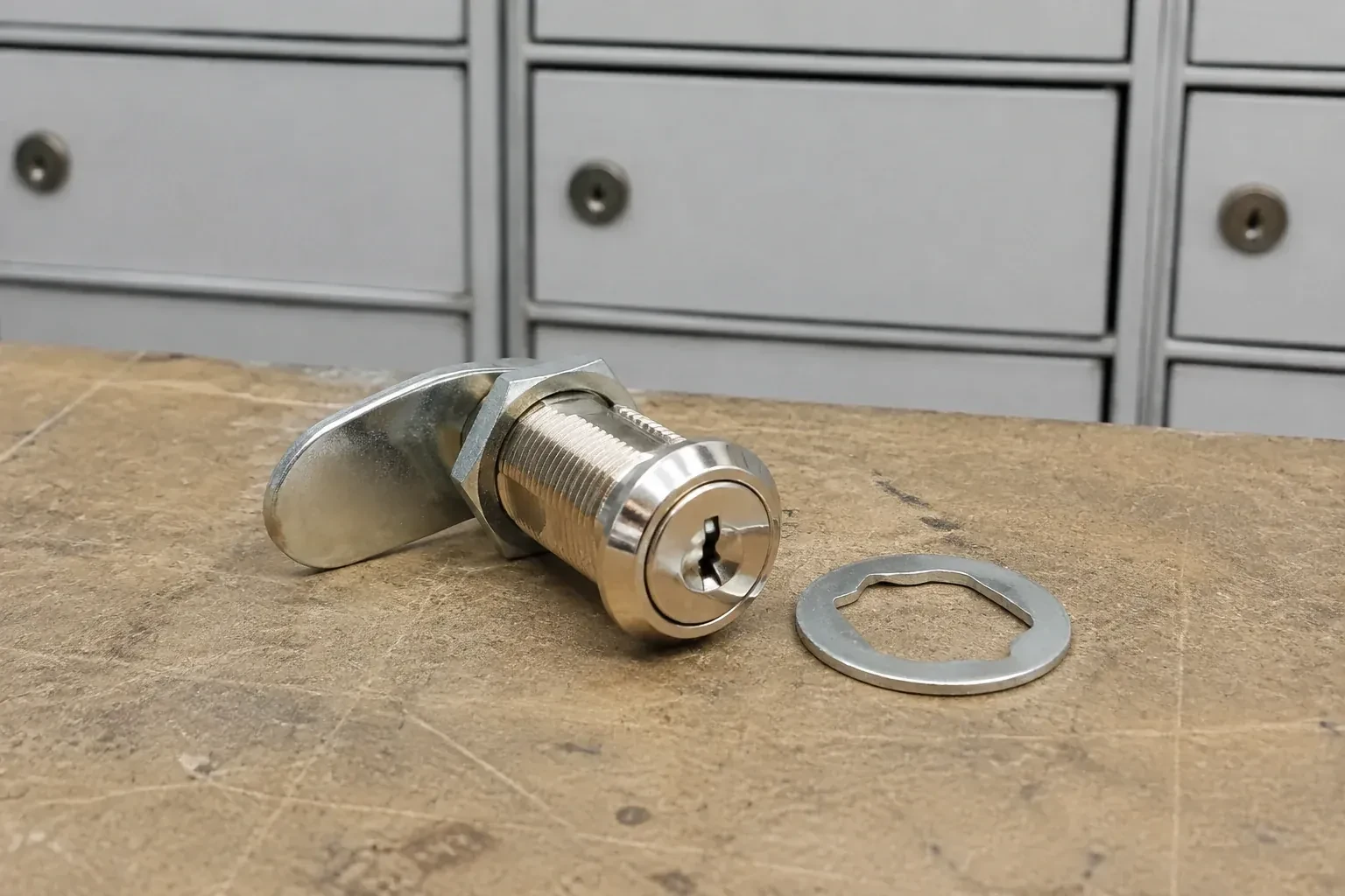 Detached threaded cam lock and mounting washer on a workbench in front of closed mail compartments. — Mailbox Lock Replacement, Kitchener