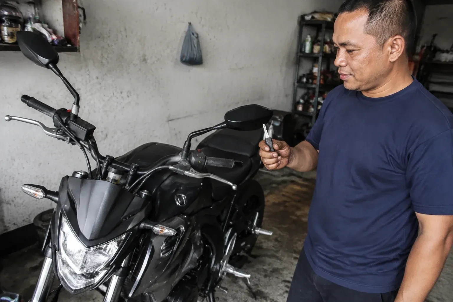 Person holding a key beside a black motorcycle in a garage. — Motorcycle & Scooter Keys, Kitchener